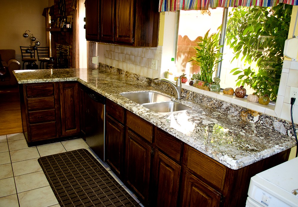Granite kitchen countertop edge with eased profile over dark wood cabinets and stainless steel sink